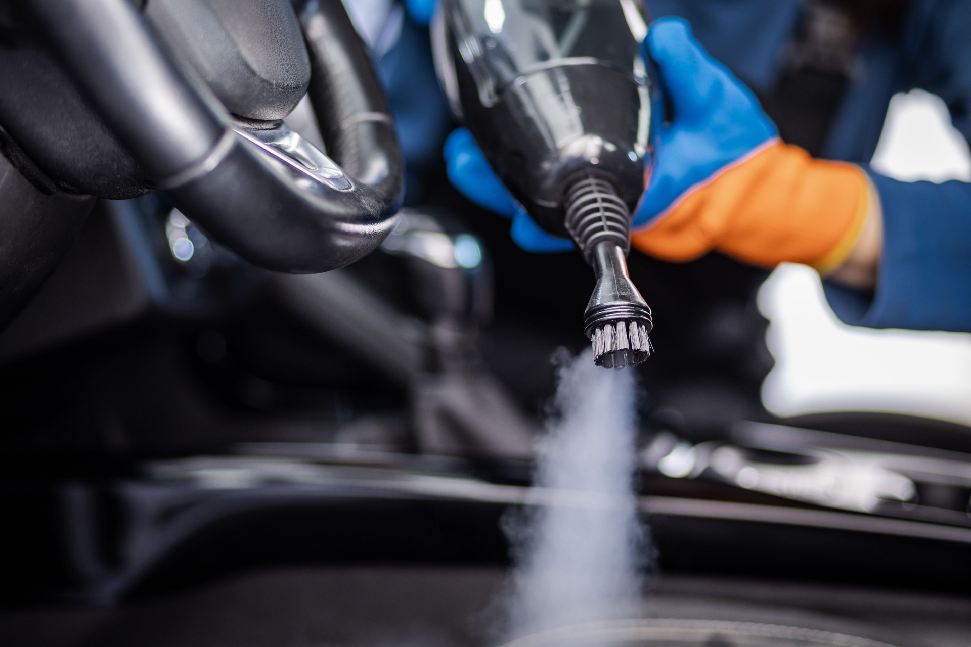 A gloved hand uses a steam cleaner to sanitize a car's interior