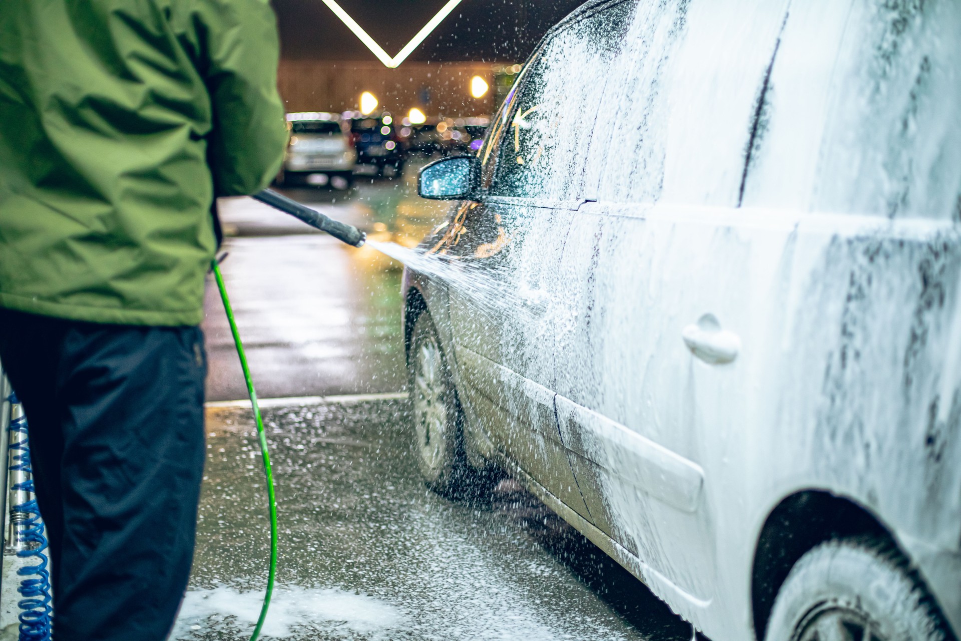 A man washes his car at a self-service car wash using a hose with pressurized water